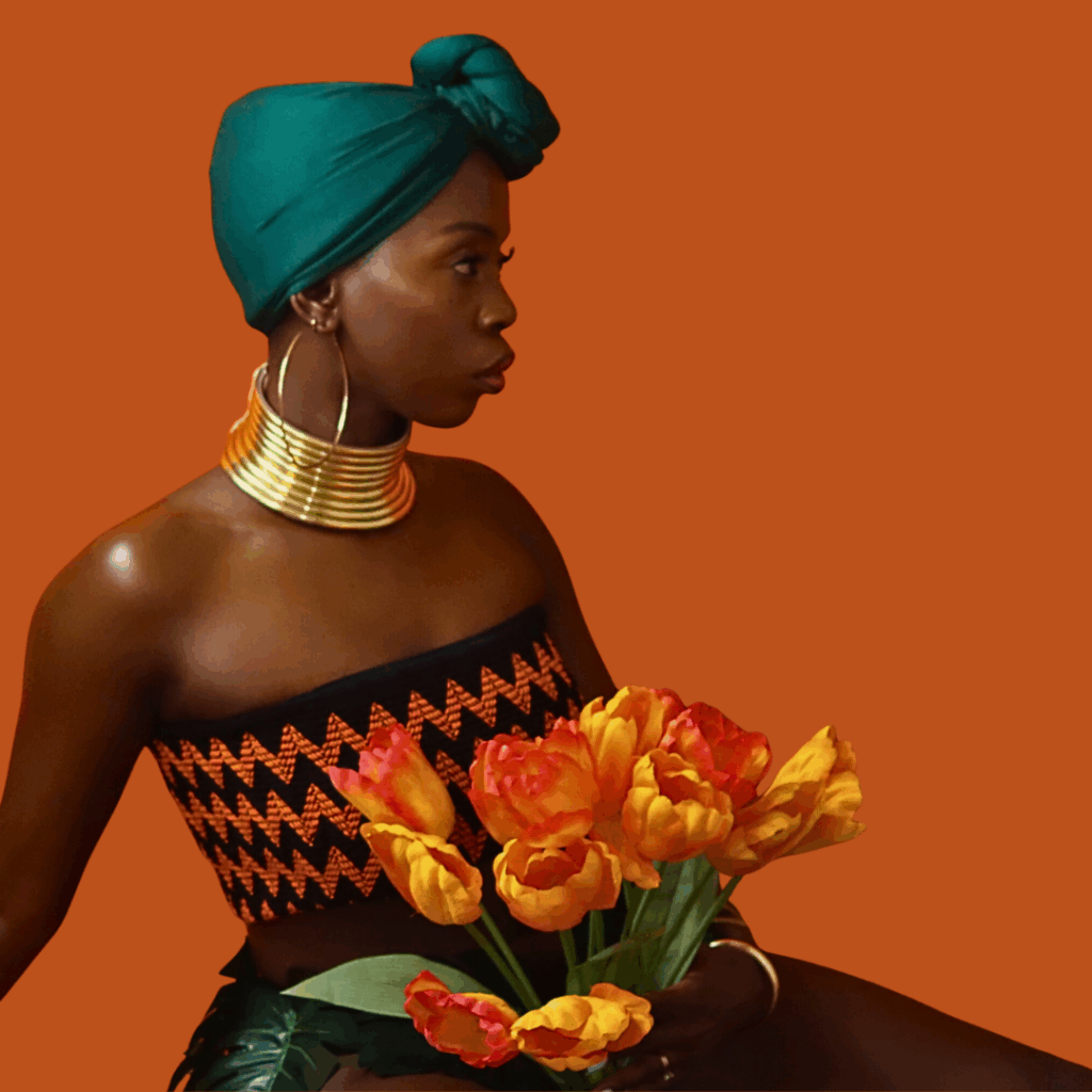 Soulful Baddie model sitting with orange flowers, looking to the side, symbolizing healing, balance, and feminine wellness journey.